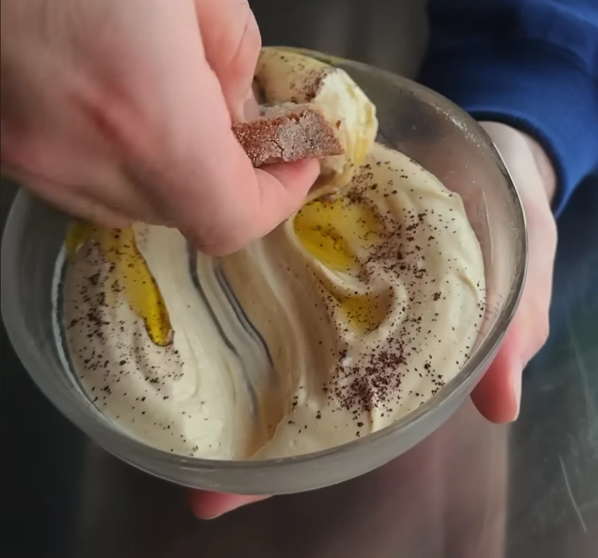 mano con pan untado de hummus de un plato